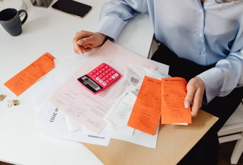 Persona sosteniendo recibos y usando una calculadora para facturación